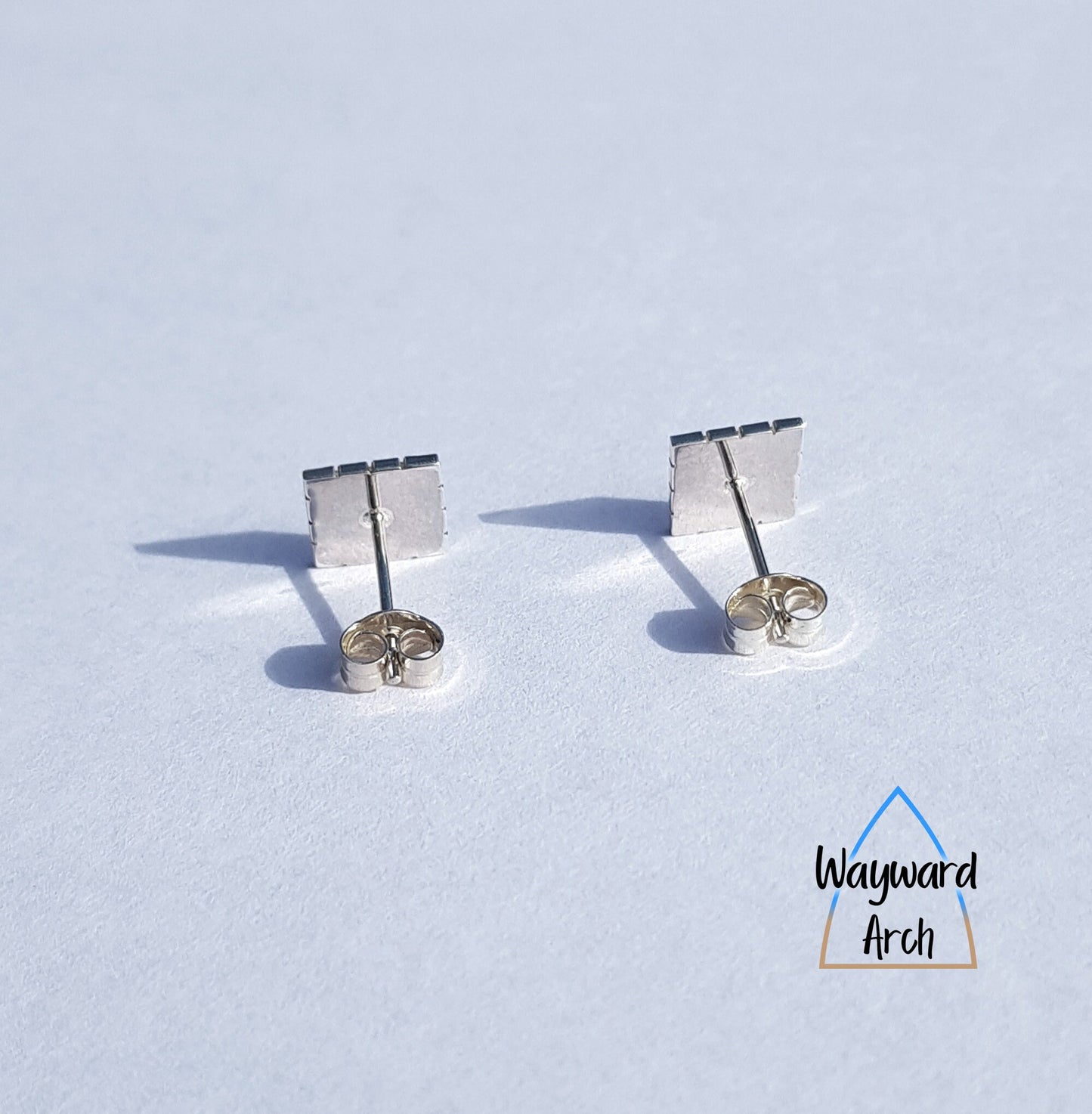 Back view of sterling silver square stud earrings with smooth polished finish and straight posts attached in the centre of the square and with butterfly scrolls