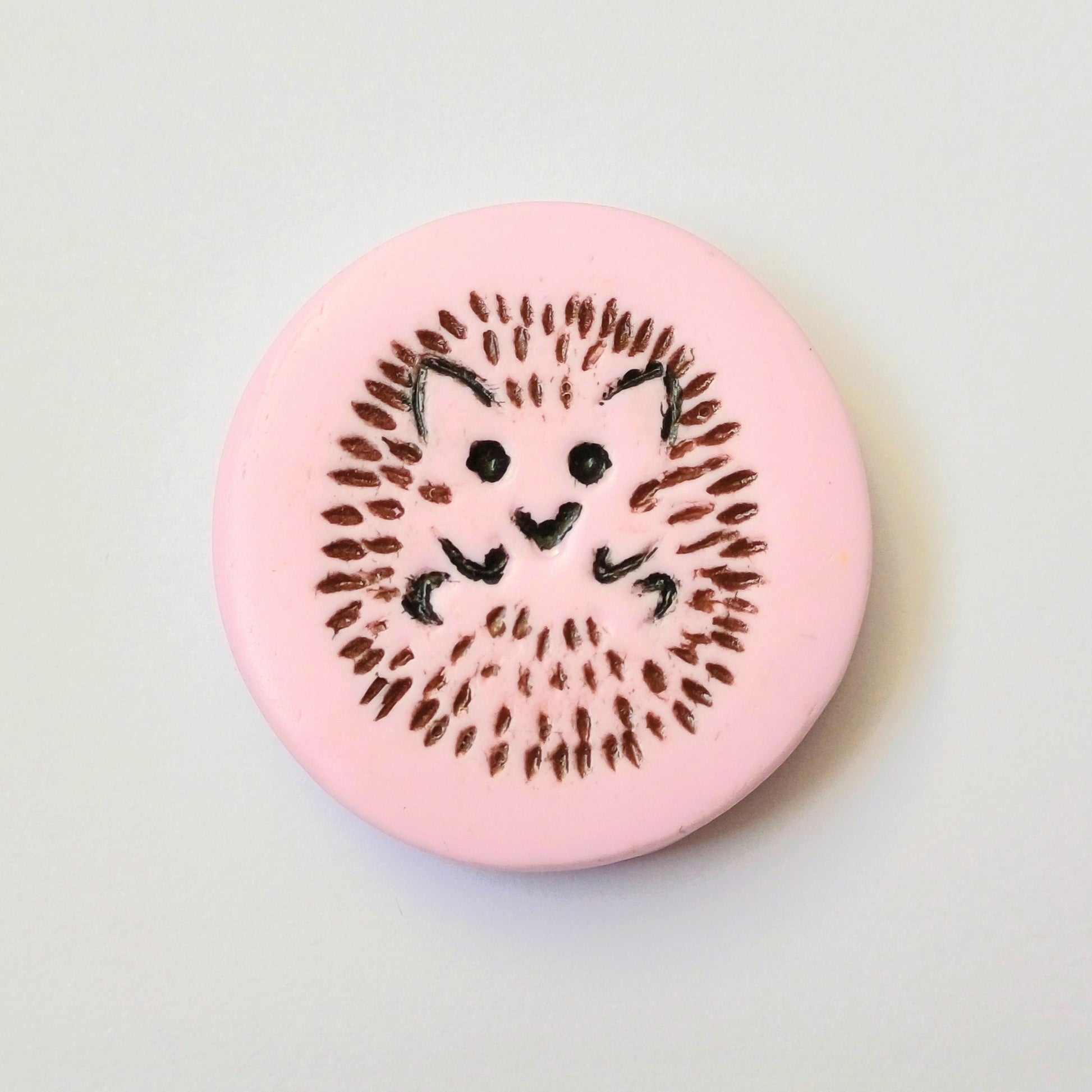 Light pink needle minder with brown and black hedgehog imprinted design.