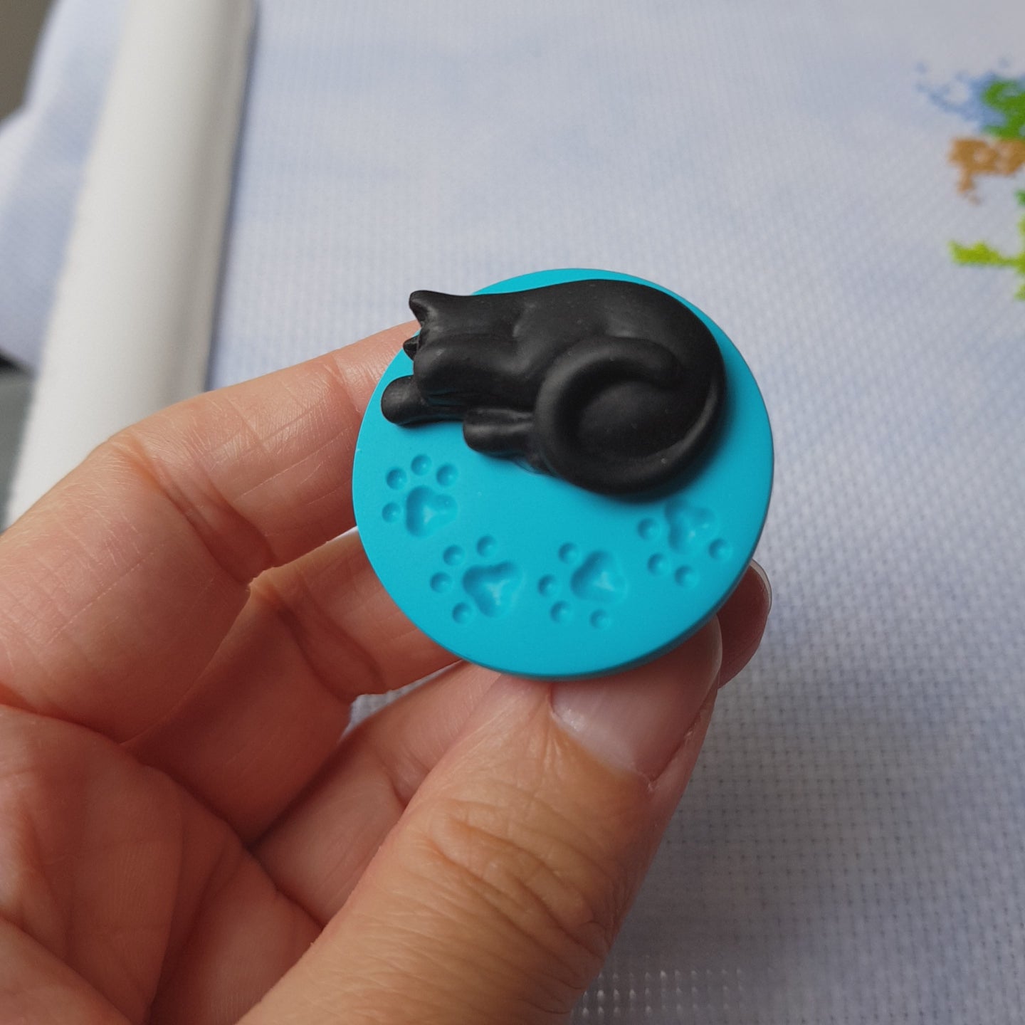 Video showing black cat on blue paw print base needle minder for cross stitching.