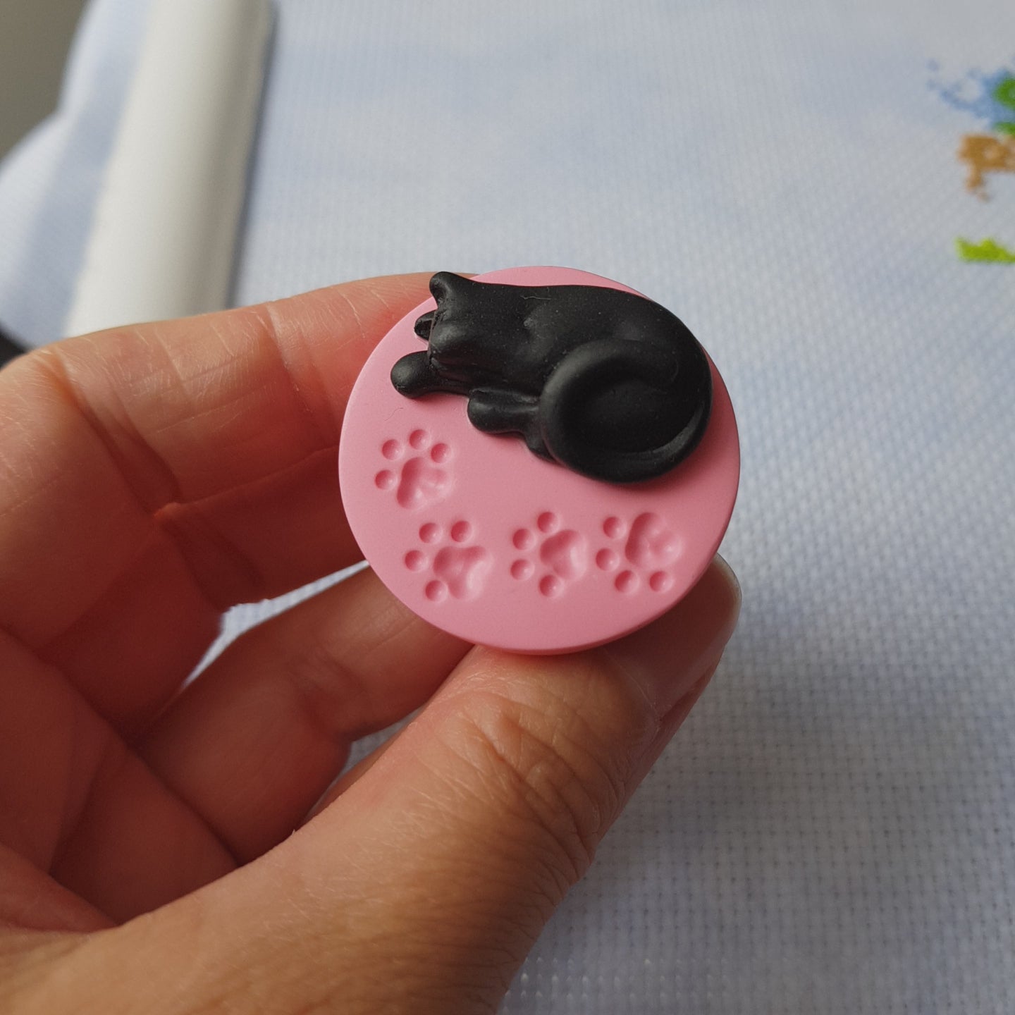 Video showing black cat on pink paw print base needle minder for cross stitching.