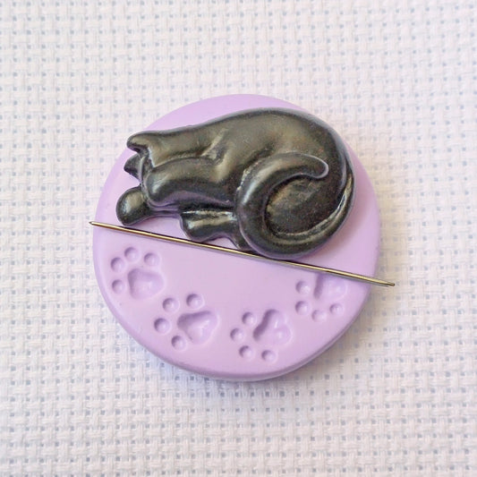 Black cat on purple paw print base needle minder for cross stitching.