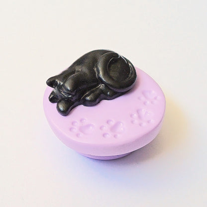 Black cat on purple paw print base needle minder for cross stitching.