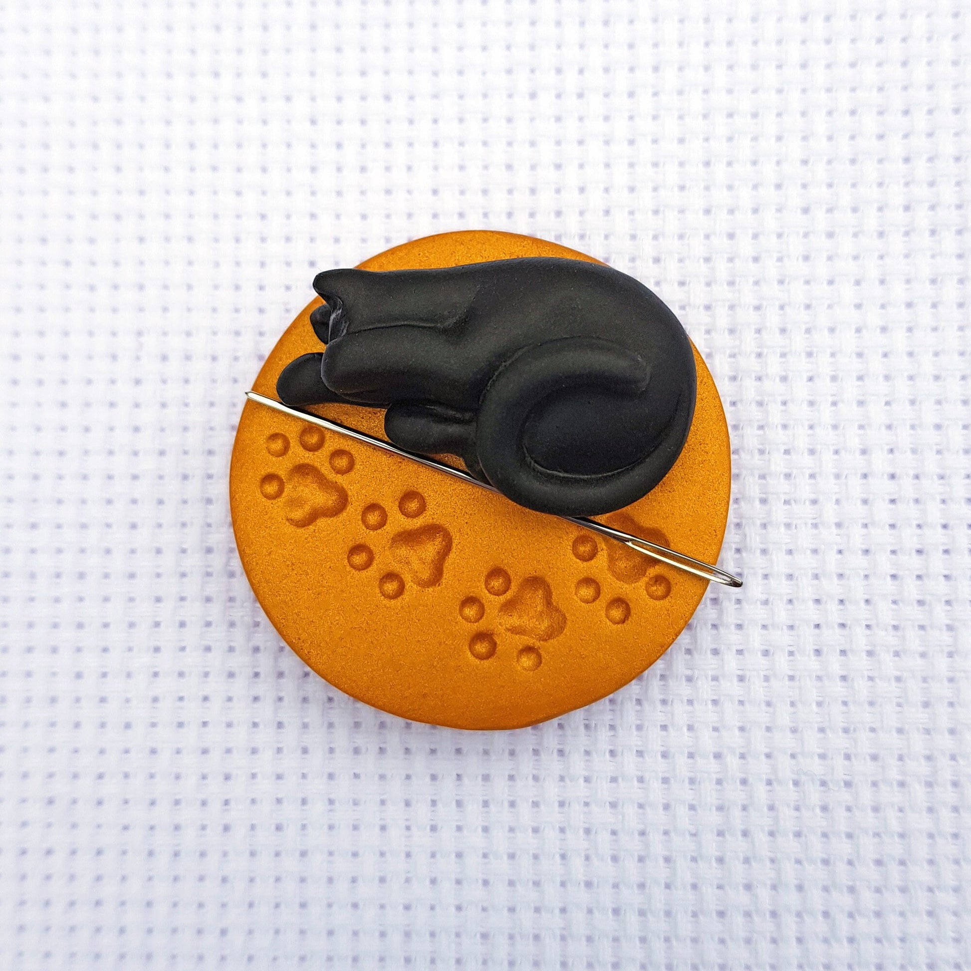 Black cat on gold paw print base needle minder for cross stitching.