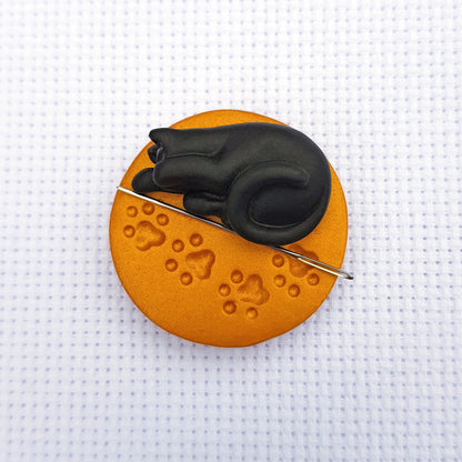 Black cat on gold paw print base needle minder for cross stitching.