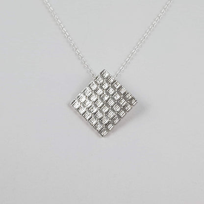 Square pendant which hangs from the corner with cross stitch aida fabric texture and dainty 18 inch chain in sterling silver.